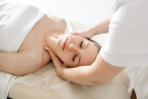 Woman lying on her back on a massage table receiving a lymphatic drainage massage from a massage therapist.