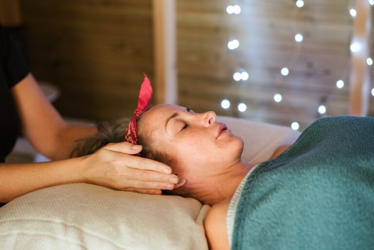 A woman lying on her back on a massage therapy table receiving reiki energy treatment.