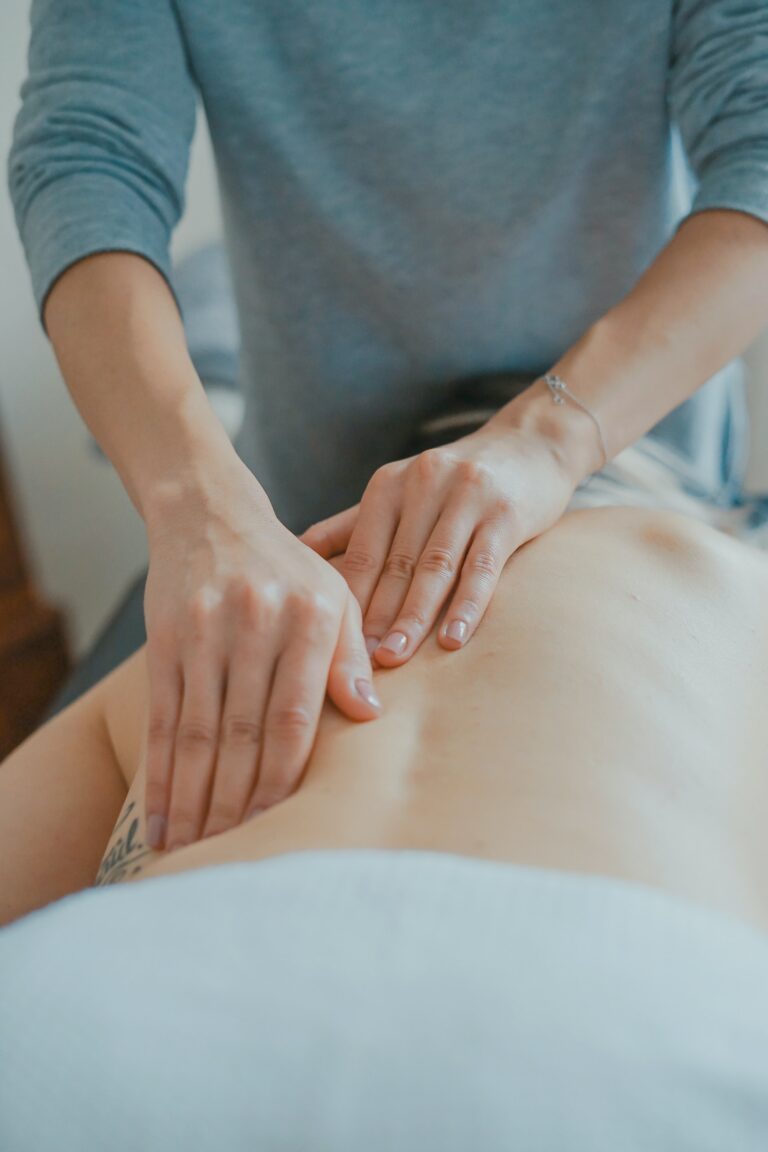 Person lying on their stomach on a massage table receiving a back massage.
