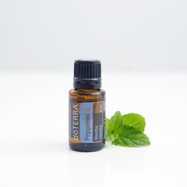 doTerra peppermint essential oil 15ml vial on a countertop next to a few mint leaves.
